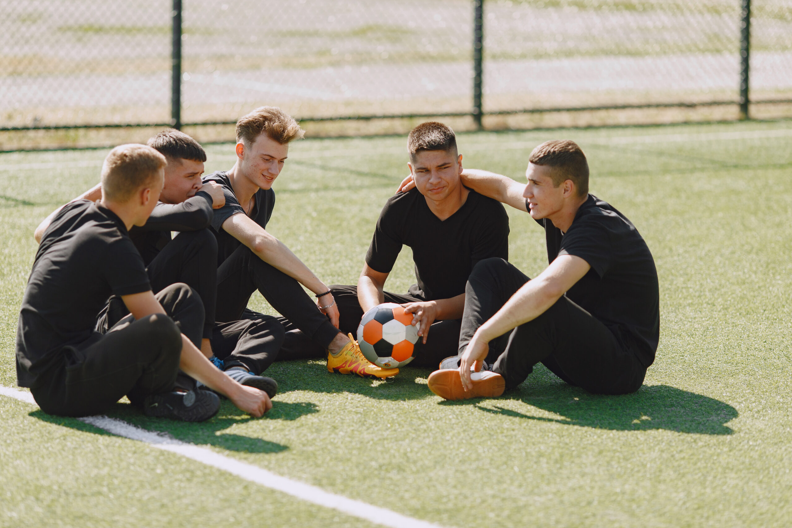 Men play socer at the park. Tournament on mini-footbal. Guy in a black sportsuits.